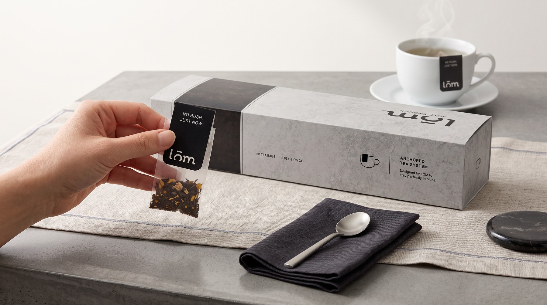 Mano sosteniendo un sobre individual de té LŌM junto a la caja, mostrando el sistema de anclaje